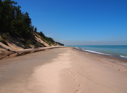 [View of the beach while standing on it looking down the length of it. The hillside is to the left and the lake to the right.]